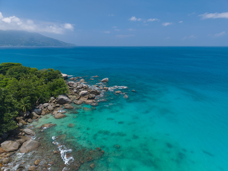 Aerial view of the rocky coastline where the vibrant turquoise water meets the lush green vegetation under the bright blue sky Vista do Mar Mahe island Seychelles. Aerial view of the rocky coastline where the vibrant turquoise water meets the lush green vegetation under the bright blue sky Vista do Mar Mahe island Seychelles.