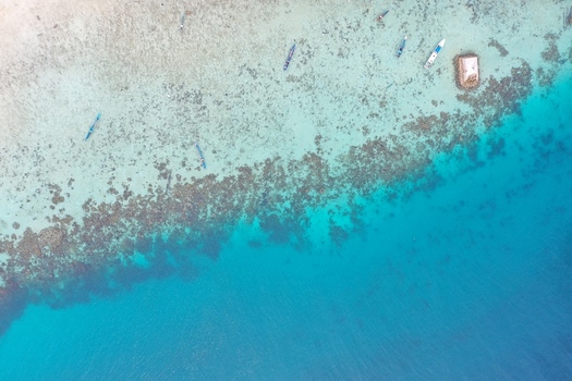 Aerial view of Pulau Maginti showing clear turquoise waters coral reefs and small traditional boats floating near the shore in Maginti South East Sulawesi Indonesia.