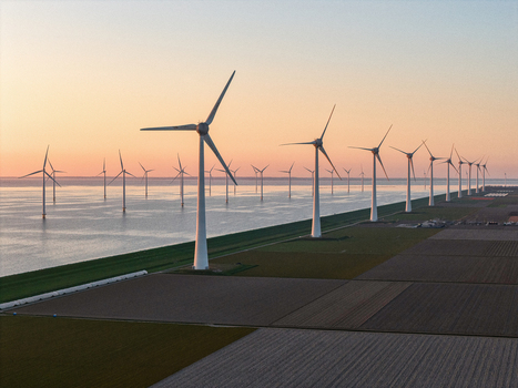 Aerial view of a large wind farm with turbines standing along a coastal dike and in the water at sunset over agricultural fields Netherlands.