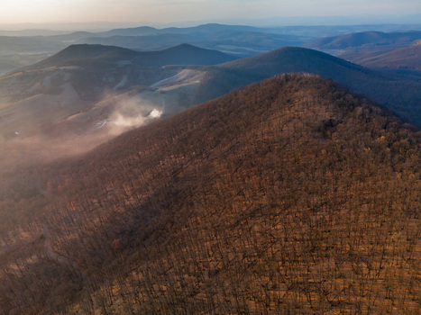 Aerial view of Ragac peak with a wisp of smoke adding a touch of mystery to the serene landscape Cerova vrchovina Banska Bystrica Region Slovakia.