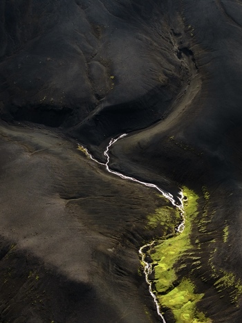 Aerial view of a silver river snaking through a black volcanic landscape accented by patches of vibrant green moss Iceland. Aerial view of a silver river snaking through a black volcanic landscape accented by patches of vibrant green moss Iceland.