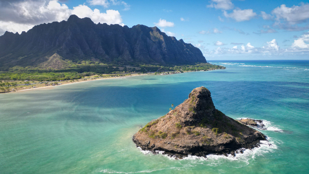 Aerial view of the iconic cone shaped islet of Mokolii rising from the turquoise waters against the backdrop of the majestic Ko olau mountain range Kaneohe Hawaii United States. Aerial view of the iconic cone shaped islet of Mokolii rising from the turquoise waters against the backdrop of the majestic Ko olau mountain range Kaneohe Hawaii United States.