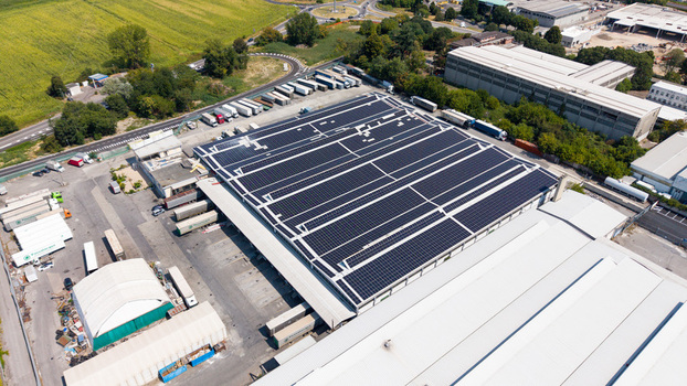 Aerial view of a logistics hub featuring a large warehouse roof covered in solar panels surrounded by parked freight trucks and transportation infrastructure Melegnano Lombardy Italy.