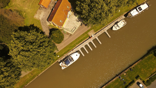 Aerial view of boats moored at a wooden dock along a canal near a building surrounded by trees in Saint Omer Hauts de France France. Aerial view of boats moored at a wooden dock along a canal near a building surrounded by trees in Saint Omer Hauts de France France.