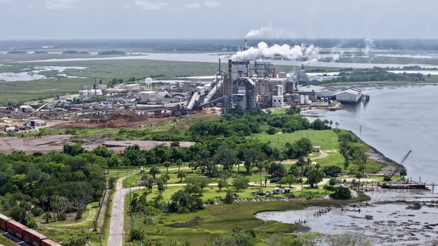 Aerial view of a towering industrial complex with billowing white smoke against serene dark waters and vibrant green marshes Fernandina Beach Florida United States. Aerial view of a towering industrial complex with billowing white smoke against serene dark waters and vibrant green marshes Fernandina Beach Florida United States.