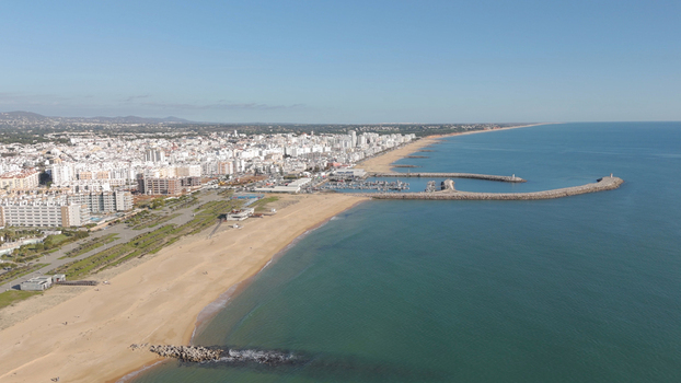 Aerial view of Vilamoura marina and the sandy coastline of Quarteira featuring calm turquoise waters a long beach and urban skyline Quarteira Faro District Portugal.