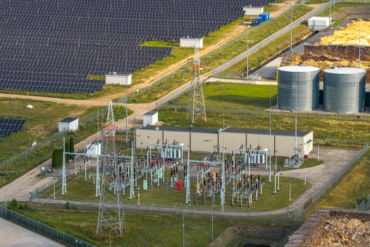 Aerial view of an electrical substation and adjacent solar farm with power lines transformers and storage tanks in a rural landscape in Poland.