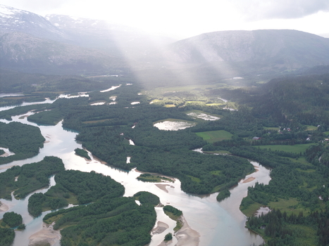 Aerial view of the braided river system with lush green islands and glacial melt water flowing through the valley surrounded by mountains in Skonseng Nordland Norway. Aerial view of the braided river system with lush green islands and glacial melt water flowing through the valley surrounded by mountains in Skonseng Nordland Norway.