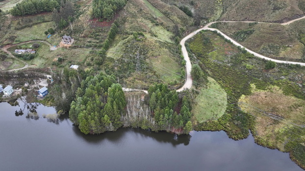 Aerial view of Corani Lake surrounded by lush green hills a winding dirt road and dense pine forests in Chapare Cochabamba Department Bolivia. Aerial view of Corani Lake surrounded by lush green hills a winding dirt road and dense pine forests in Chapare Cochabamba Department Bolivia.