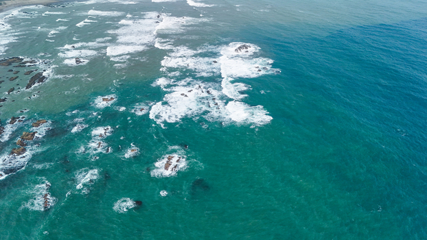 Aerial view of ocean waves crashing against rocky formations along the coastline of Indonesia. Aerial view of ocean waves crashing against rocky formations along the coastline of Indonesia.