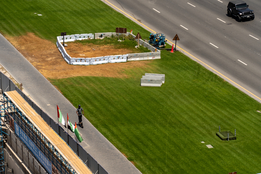 Aerial view of a roadside green lawn with construction barriers a person on a scooter and UAE flags next to a highway in Dubai Dubai United Arab Emirates. Aerial view of a roadside green lawn with construction barriers a person on a scooter and UAE flags next to a highway in Dubai Dubai United Arab Emirates.