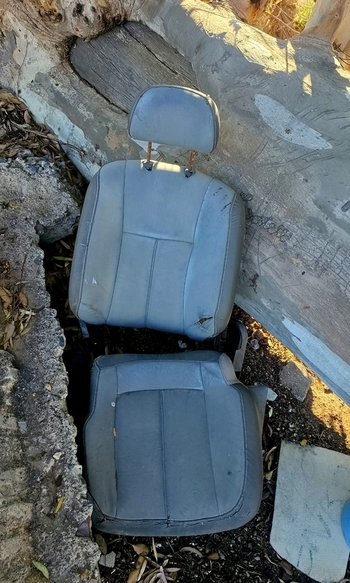 View of an abandoned and worn car seat lying on the ground with exposed frame and damaged fabric in an outdoor setting in Ladismith Western Cape South Africa. View of an abandoned and worn car seat lying on the ground with exposed frame and damaged fabric in an outdoor setting in Ladismith Western Cape South Africa.