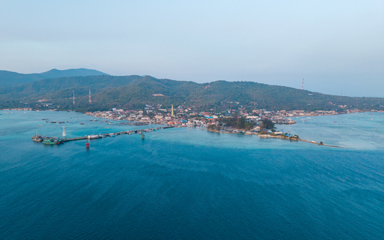 Aerial view of Karimunjawa town square and the long pier extending into the turquoise sea surrounded by lush green hills and clear blue water in Karimunjawa Central Java Indonesia. Aerial view of Karimunjawa town square and the long pier extending into the turquoise sea surrounded by lush green hills and clear blue water in Karimunjawa Central Java Indonesia.