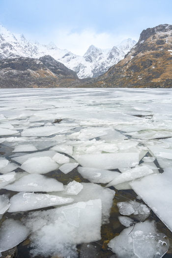 View of ice floes floating on a frozen lake with snow capped mountains in the background under an overcast sky in Leknes Lofoten Norway.