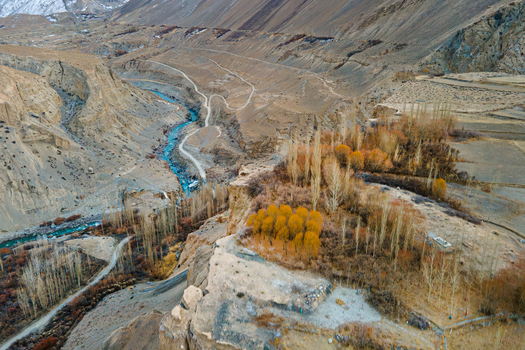 Aerial view of the aquamarine river winding through the rugged arid landscape contrasting with the golden hues of the trees in Chapursan Valley Hunza Nagar Gilgit Pakistan. Aerial view of the aquamarine river winding through the rugged arid landscape contrasting with the golden hues of the trees in Chapursan Valley Hunza Nagar Gilgit Pakistan.
