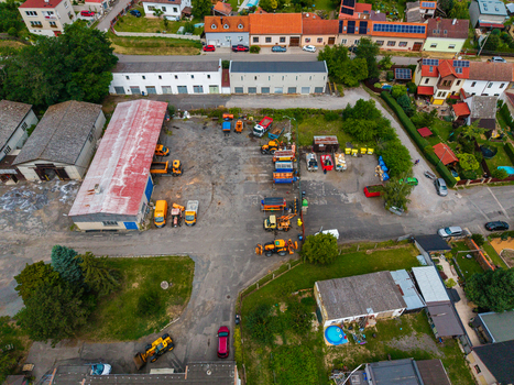 Aerial view of a construction yard featuring yellow heavy machinery trucks and equipment surrounded by residential houses and green spaces in Zebrak Central Bohemian Region Czechia. Aerial view of a construction yard featuring yellow heavy machinery trucks and equipment surrounded by residential houses and green spaces in Zebrak Central Bohemian Region Czechia.