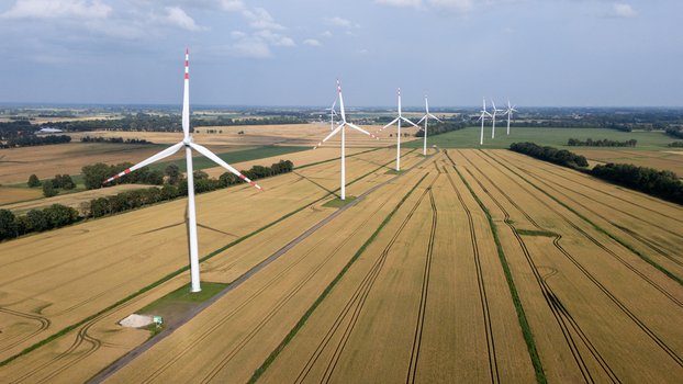 Aerial view of wind turbines standing in a vast golden wheat field under a clear blue sky in Gdansk Pomeranian Voivodeship Poland. Aerial view of wind turbines standing in a vast golden wheat field under a clear blue sky in Gdansk Pomeranian Voivodeship Poland.