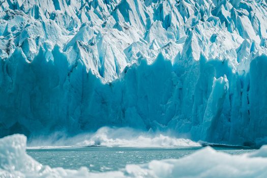 View of the massive jagged blue ice wall of the Perito Moreno Glacier rising above turquoise water with ice chunks in the foreground in Perito Moreno Santa Cruz Province Argentina. View of the massive jagged blue ice wall of the Perito Moreno Glacier rising above turquoise water with ice chunks in the foreground in Perito Moreno Santa Cruz Province Argentina.