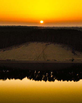 Aerial view of the Lielupe White Dune at sunrise featuring a sandy dune covered in pine trees reflected in the calm river water in Jurmala Latvia. Aerial view of the Lielupe White Dune at sunrise featuring a sandy dune covered in pine trees reflected in the calm river water in Jurmala Latvia.