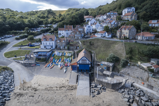 Aerial view of the Runswick Bay lifeboat station with colorful kayaks stored on the slipway and historic houses nestled on the hillside in Runswick Bay England United Kingdom.