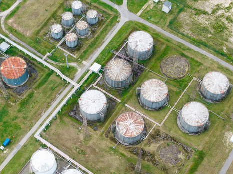 Aerial view of an industrial oil storage facility with large cylindrical metal tanks connected by pipelines surrounded by green grass in Olaine parish Olaine Municipality Latvia.