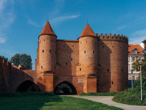 View of the historic red brick Warsaw Barbican with its defensive towers and arched gateway set against a clear blue sky in Warsaw Masovian Voivodeship Poland. View of the historic red brick Warsaw Barbican with its defensive towers and arched gateway set against a clear blue sky in Warsaw Masovian Voivodeship Poland.