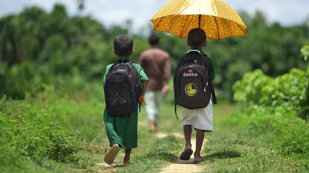 View of schoolboys walking on a path with an umbrella Bangladesh.