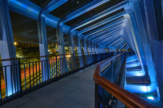 View of the modern JPO Pandanaran pedestrian bridge at night featuring geometric blue LED lighting and light trails from traffic below in Semarang Central Java Indonesia.