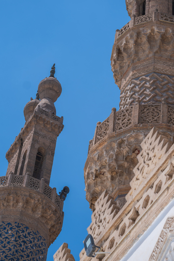 View of the intricate stone carvings and ornate minarets of Al Azhar Mosque against a clear blue sky in Cairo Egypt. View of the intricate stone carvings and ornate minarets of Al Azhar Mosque against a clear blue sky in Cairo Egypt.