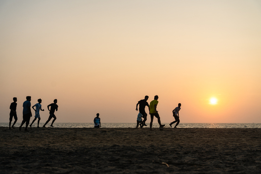 View of silhouettes of young men playing football on a sandy beach at sunset with the sun glowing over the ocean horizon Galle Southern Province Sri Lanka.