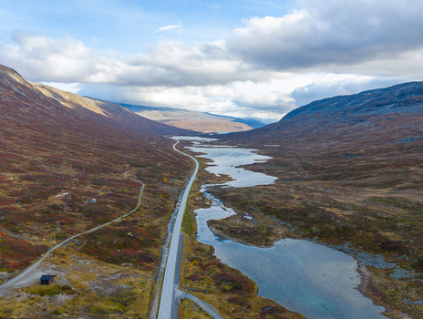 Aerial view of Skjakvegen winding through a dramatic valley with lakes mountains and autumn colored vegetation in Skjak Innlandet Norway. Aerial view of Skjakvegen winding through a dramatic valley with lakes mountains and autumn colored vegetation in Skjak Innlandet Norway.