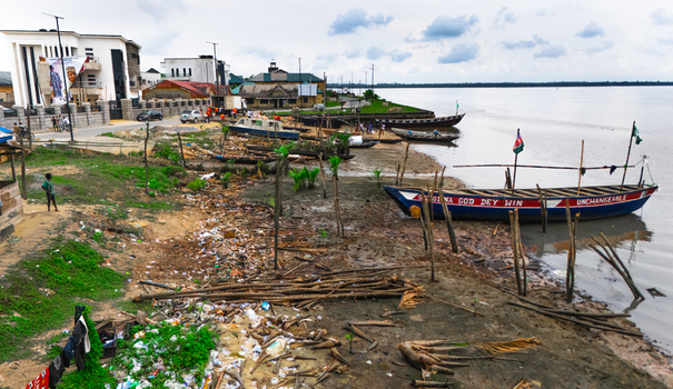 Aerial view of wooden boats moored along the riverbank with scattered debris and buildings in the background in Minima Rivers Nigeria.