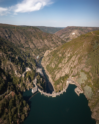 Aerial view of Encoro de Santo Estevo dam situated in a deep river canyon surrounded by steep forested hills under a clear blue sky in Ourense Ourense Spain. Aerial view of Encoro de Santo Estevo dam situated in a deep river canyon surrounded by steep forested hills under a clear blue sky in Ourense Ourense Spain.