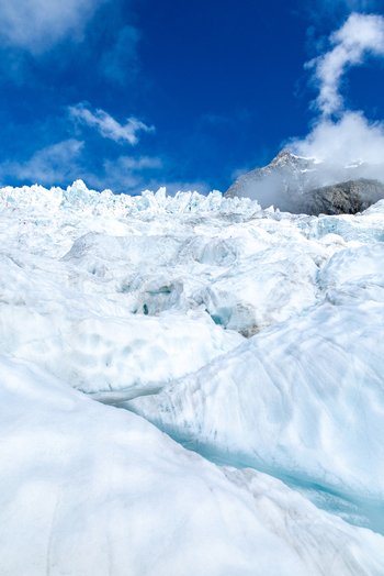 View of the icy glacier s bright white expanse under a vibrant blue sky meeting a distant snow capped mountain peak Franz Josef Glacier West Coast Region New Zealand. View of the icy glacier s bright white expanse under a vibrant blue sky meeting a distant snow capped mountain peak Franz Josef Glacier West Coast Region New Zealand.
