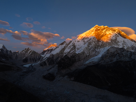 Aerial view of the Himalayan mountain range at golden hour with snow capped peaks glowing in the sunset light deep shadows in the valleys and wispy clouds in the blue sky Nepal.