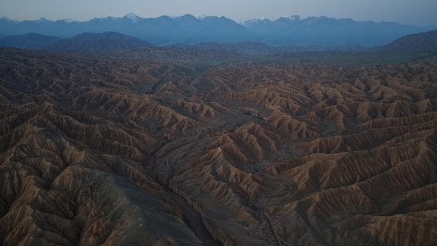 Aerial view of the rugged badlands and deep canyons of Issyk Kul with dramatic eroded ridges and snow capped mountains in the distance in Issyk Kul Region Kyrgyzstan. Aerial view of the rugged badlands and deep canyons of Issyk Kul with dramatic eroded ridges and snow capped mountains in the distance in Issyk Kul Region Kyrgyzstan.