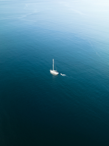 Aerial view of a lone sailboat adrift in the vast deep blue expanse its white sails contrasting against the dark waters Goro South Province New Caledonia. Aerial view of a lone sailboat adrift in the vast deep blue expanse its white sails contrasting against the dark waters Goro South Province New Caledonia.