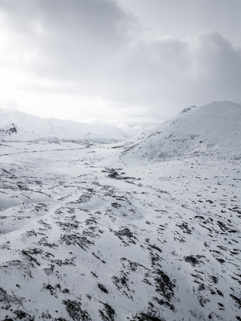 Aerial view of a vast snowy mountain valley with rocky slopes under an overcast sky in Ersfjord Troms Norway. Aerial view of a vast snowy mountain valley with rocky slopes under an overcast sky in Ersfjord Troms Norway.