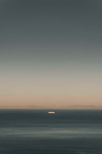 View of a distant cruise ship sailing on the calm sea during sunset with mountains visible on the horizon in Moskenes Nordland Norway.