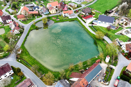 Aerial view of a central village pond surrounded by traditional houses with red tiled roofs and lush green gardens in Lonnerstadt Bayern Germany. Aerial view of a central village pond surrounded by traditional houses with red tiled roofs and lush green gardens in Lonnerstadt Bayern Germany.