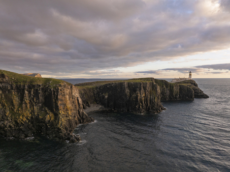Aerial view of Neist Point Lighthouse perched on dramatic sea cliffs at sunset with golden light reflecting on the water and rugged coastal landscape Scotland United Kingdom. Aerial view of Neist Point Lighthouse perched on dramatic sea cliffs at sunset with golden light reflecting on the water and rugged coastal landscape Scotland United Kingdom.