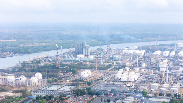 Aerial view of an industrial oil refinery complex with storage tanks processing towers and a flare stack situated along a river in Cilacap Central Java Indonesia. Aerial view of an industrial oil refinery complex with storage tanks processing towers and a flare stack situated along a river in Cilacap Central Java Indonesia.