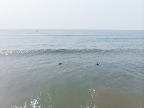 Aerial view of two surfers in the ocean on a sunny day at Agonda beach in south Goa India.