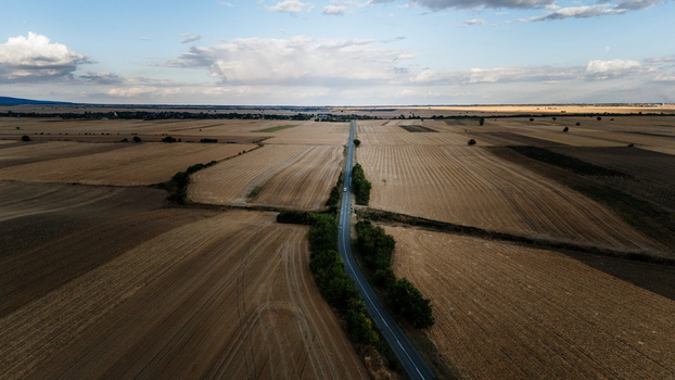 Aerial view of a straight road cutting through vast harvested agricultural fields in the rural landscape under a cloudy sky in Veliki Radinci Vojvodina Serbia.
