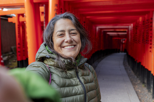 View of a smiling woman taking a selfie in front of the red Senbon Torii Thousand Torii Gates at Fushimi Inari Shrine Kyoto Kyoto Japan.