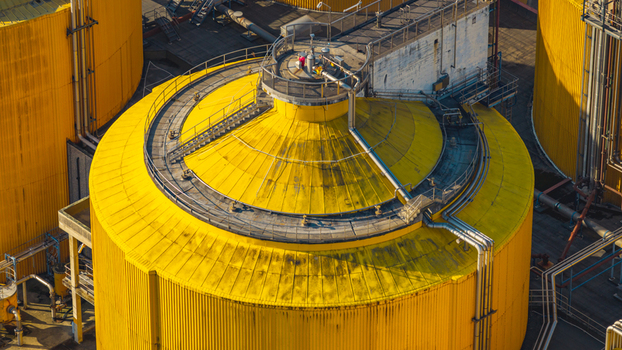 Aerial view of a large yellow anaerobic digestion tank with industrial pipelines and circular access platforms at a wastewater treatment plant in Italy. Aerial view of a large yellow anaerobic digestion tank with industrial pipelines and circular access platforms at a wastewater treatment plant in Italy.