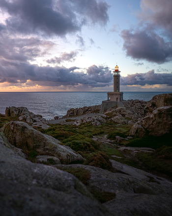 View of Faro de Punta Nariga lighthouse standing on a rugged rocky coastline under a dramatic cloudy sky at sunset in Malpica A Coruna Spain. View of Faro de Punta Nariga lighthouse standing on a rugged rocky coastline under a dramatic cloudy sky at sunset in Malpica A Coruna Spain.