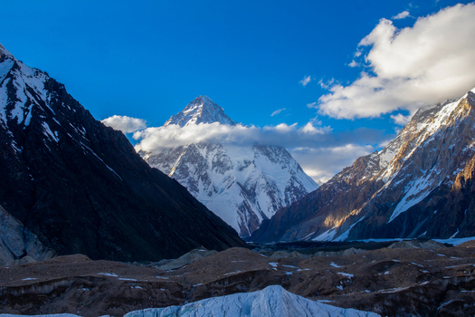 View of the snow capped peak of K2 mountain surrounded by rugged ridges and white clouds under a clear blue sky Skardu Gilgit Pakistan.
