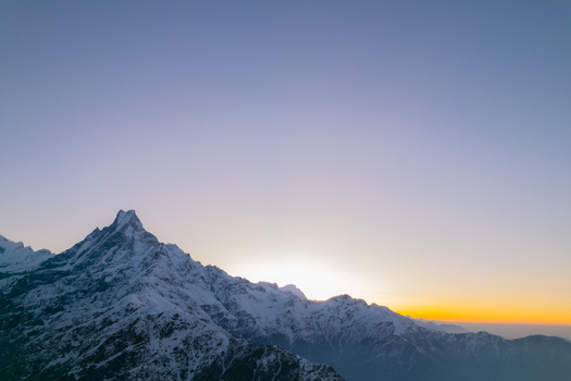 Aerial view of the snow covered peak of Machapuchare at sunrise with golden light illuminating the Himalayan range in Nepal.