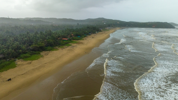 Aerial view of Gokarna beach with golden sands lush palm trees and rolling waves under a cloudy sky in Gokarna Karnataka India.